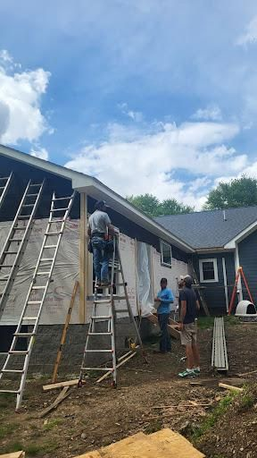 Construction workers siding a house, using ladders. Sunny day, blue sky.