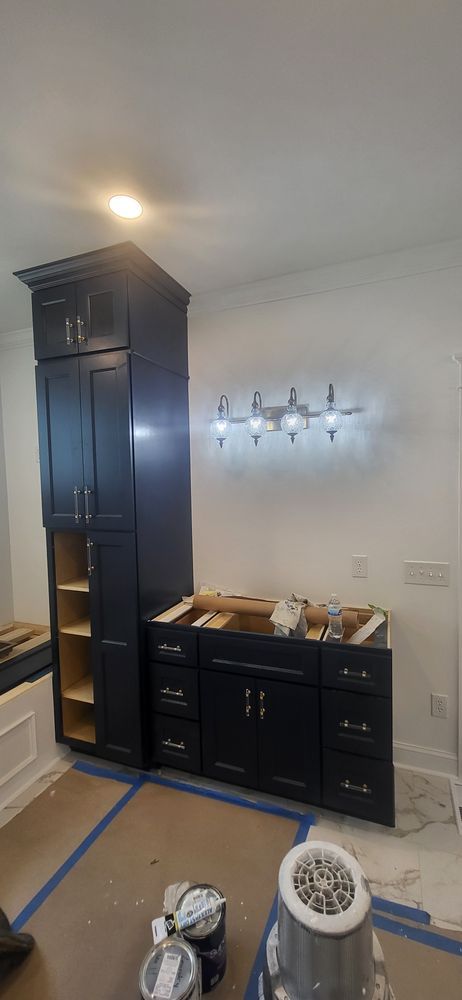 A dark blue bathroom vanity and tall cabinet against a white wall with a light fixture.