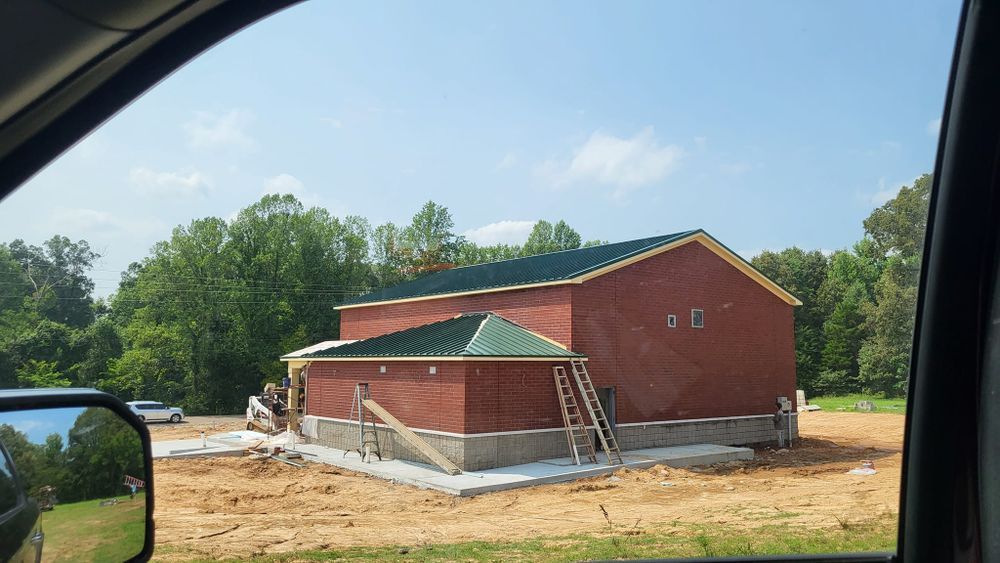 Construction of a brick building with green roofing on a concrete foundation, in an outdoor setting.