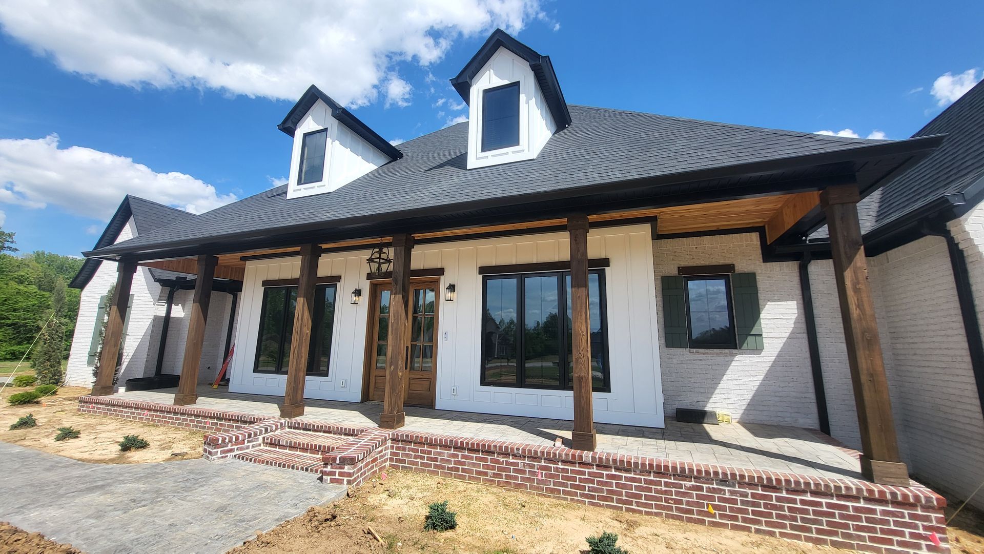 House with white brick, black trim, wood porch, and blue sky.
