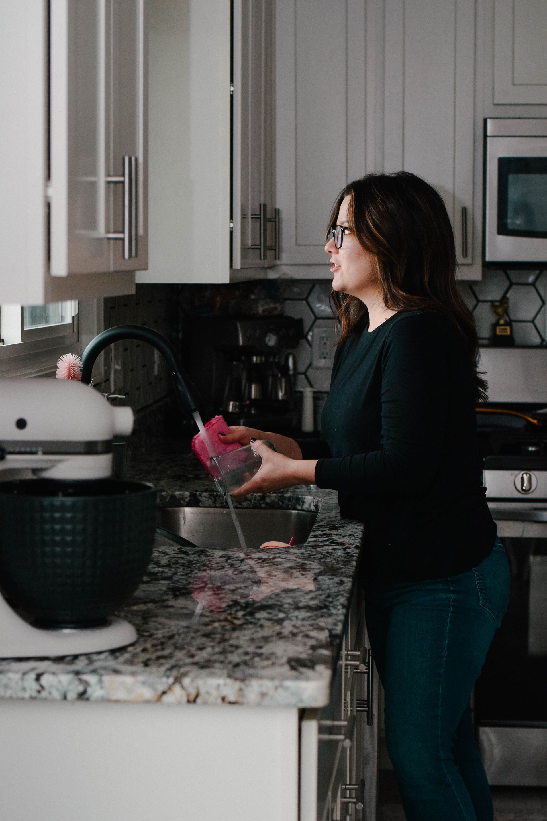 Woman in kitchen washing a bowl, near a stand mixer, and a sink.