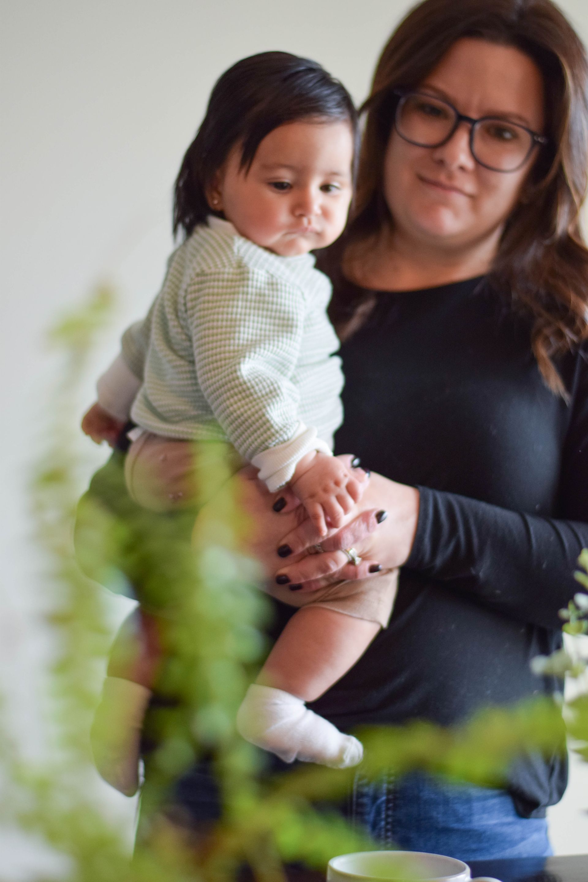 Woman holding a baby, both looking down. The woman wears glasses and a black shirt.
