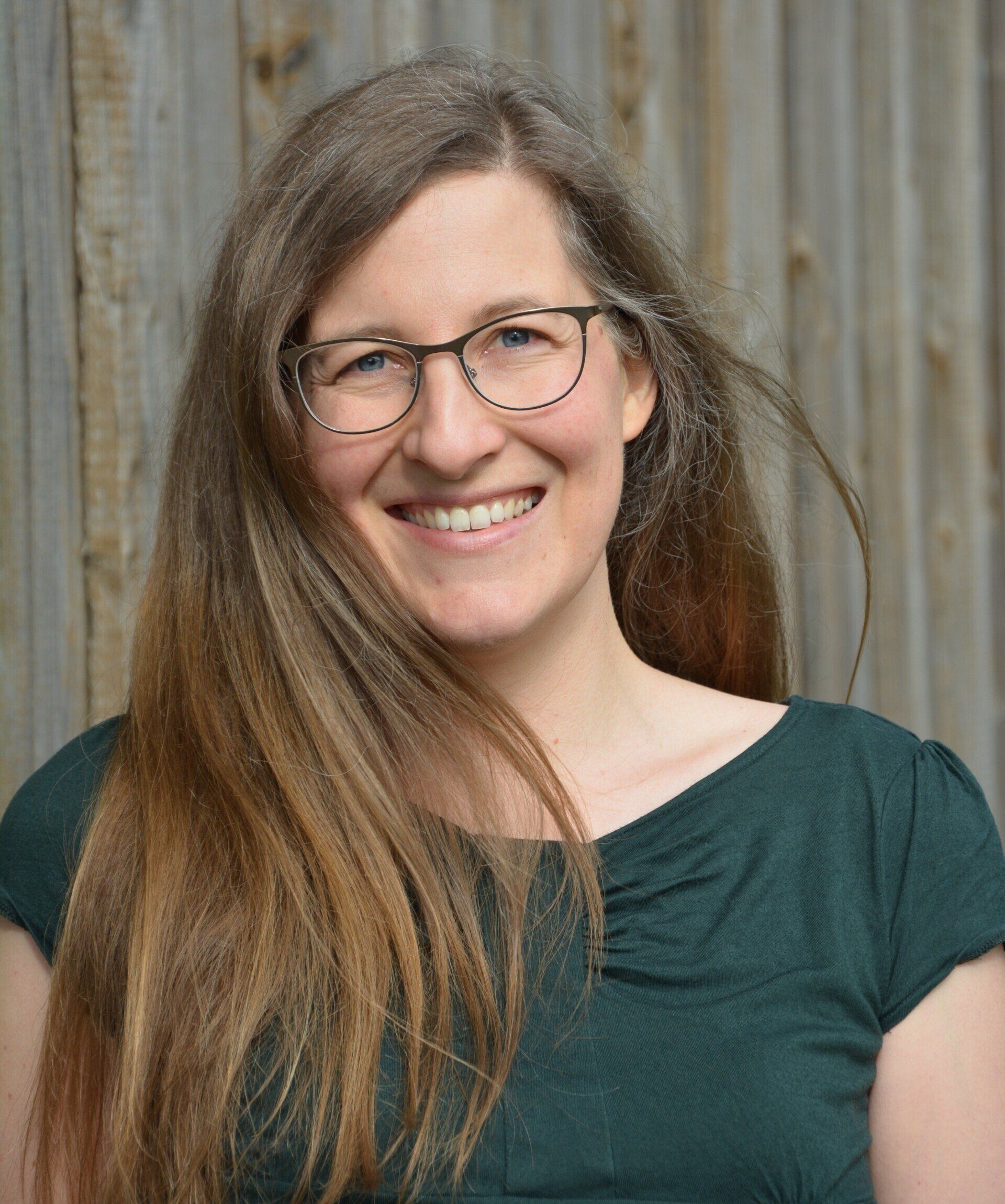 Eine Frau mit Brille und grünem Hemd lächelt