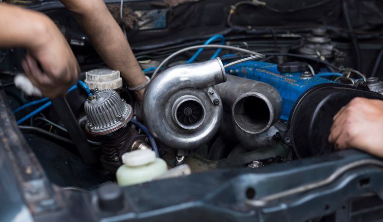 Una persona está trabajando en el motor de un automóvil con el capó abierto.