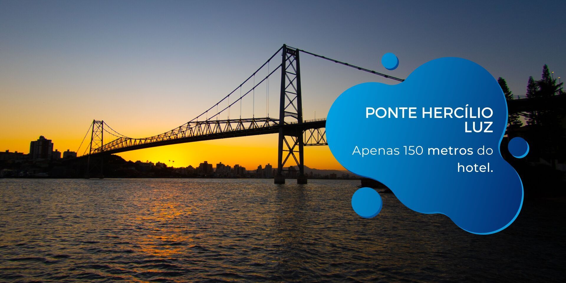 Ponte Hercílio Luz ao pôr do sol sobre a água, com balão de texto azul anunciando a 150 metros do hotel.