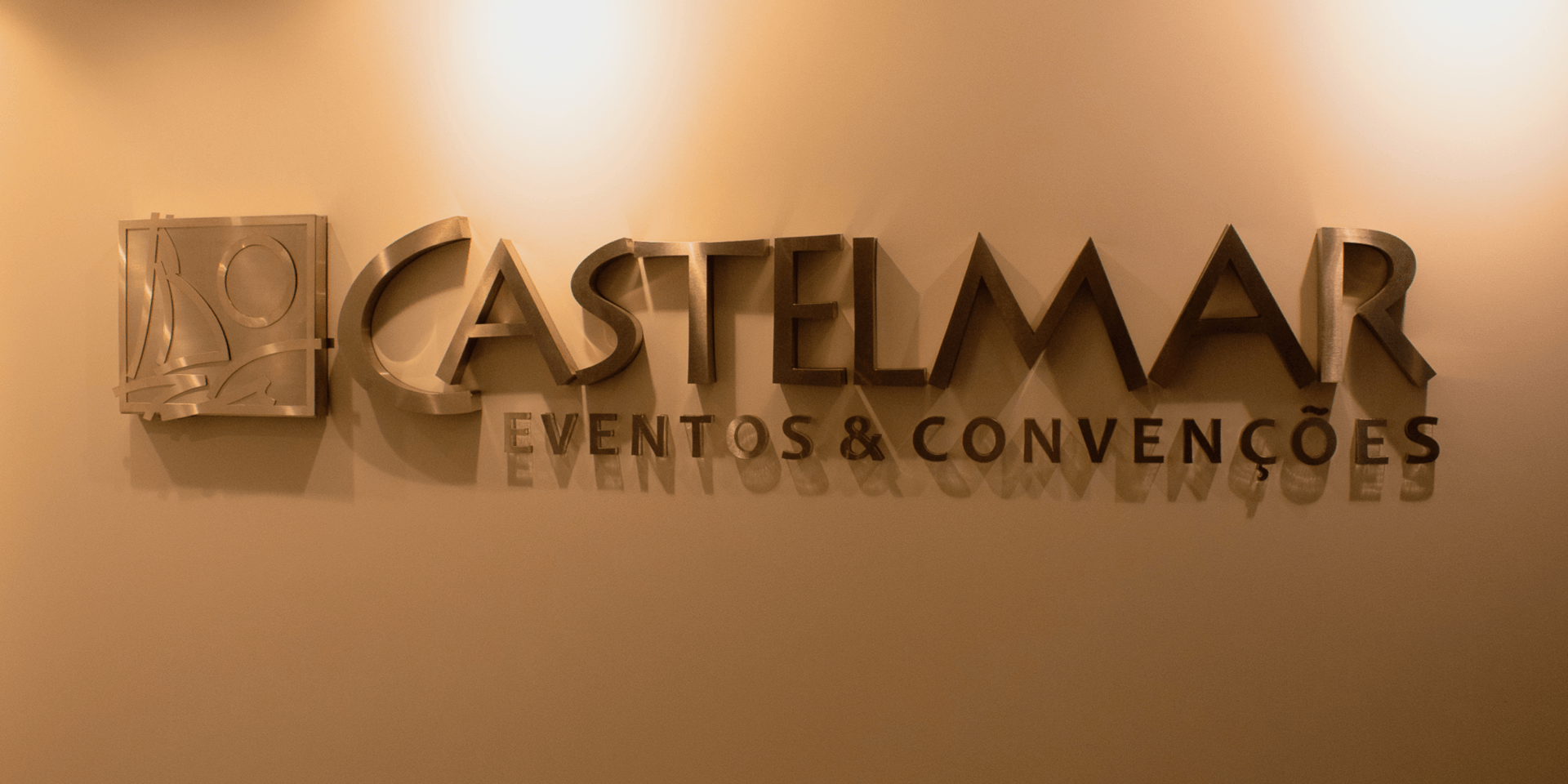 CASTELMAR Eventos & Convenções logo em uma parede bege com letras metálicas e emblem