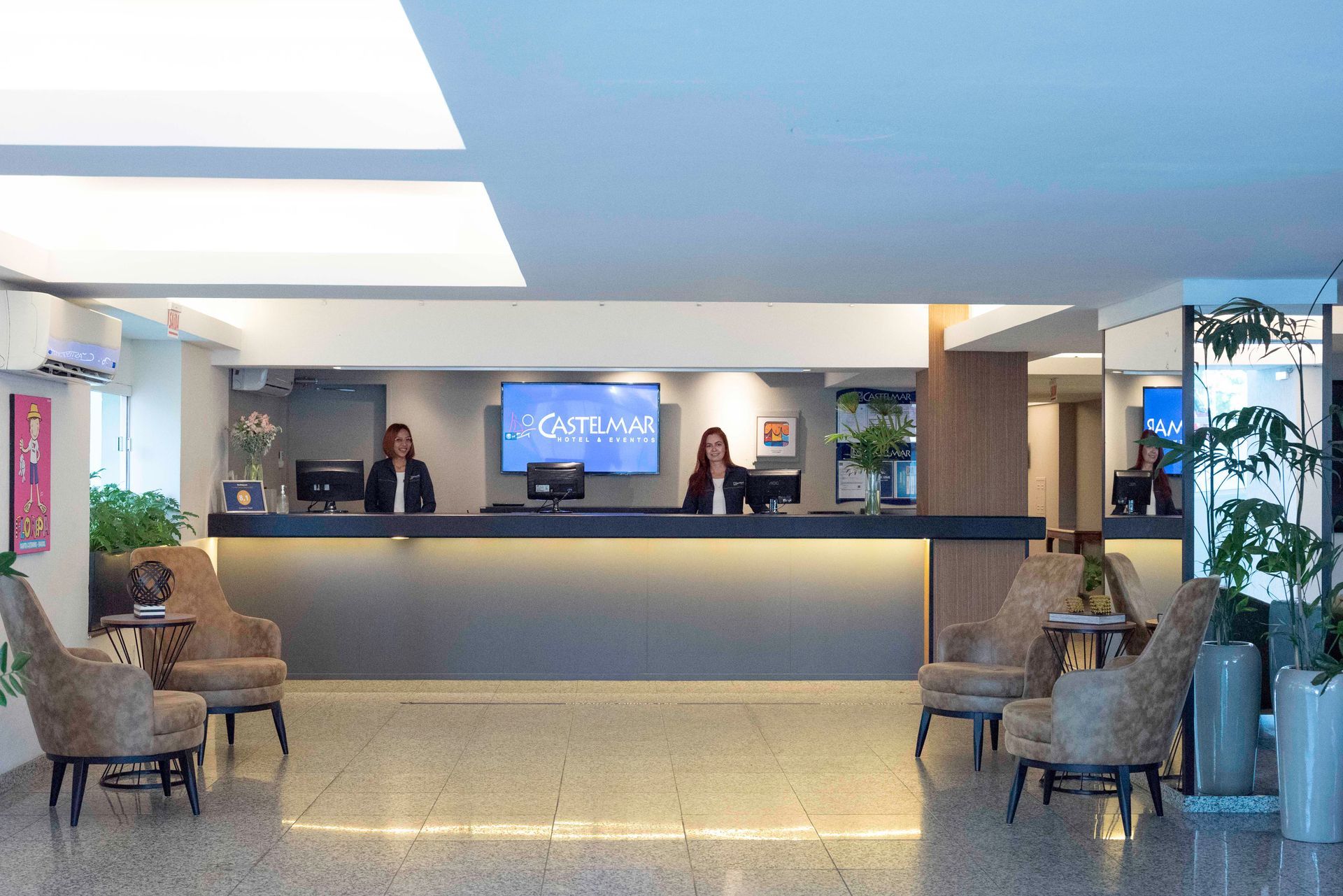 Hall de entrada do hotel com recepção, área de estar e balcão de atendimento com iluminação azul.