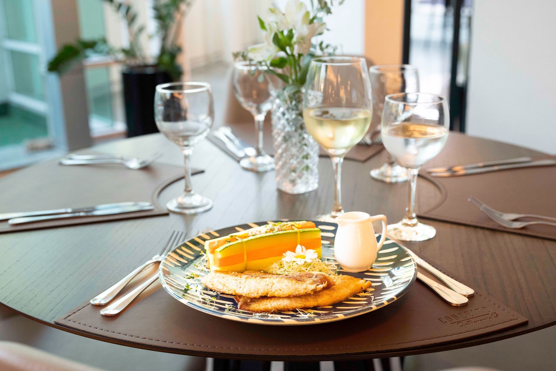 Conjunto de mesa de jantar formal com pratos, taças de vinho, talheres e um prato de sobremesa com frutas como centro de mesa.