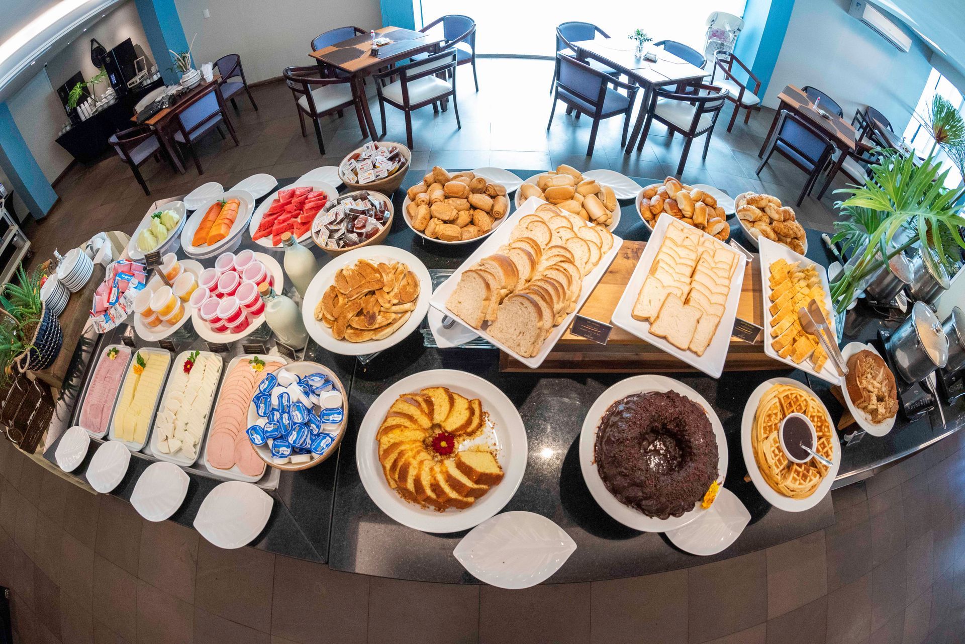 Mesa de buffet com uma variedade de bolos, doces e sobremesas em uma sala de jantar iluminada.
