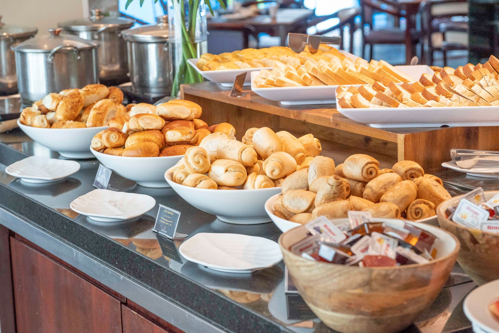 Buffet de café da manhã com doces, pãezinhos e sobremesas em bandejas e tigelas.