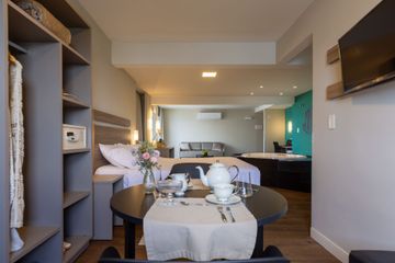 Quarto de hotel moderno com cama de casal, mesa para alimentaçao, TV e piso de madeira escura, banheira de hidromassagem