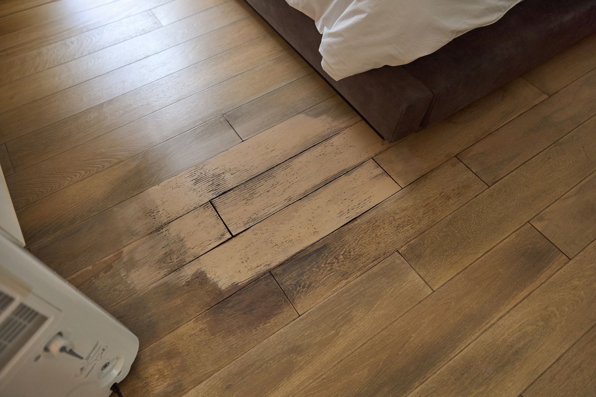 Wooden floor with dark staining near a bed and an air conditioning unit.
