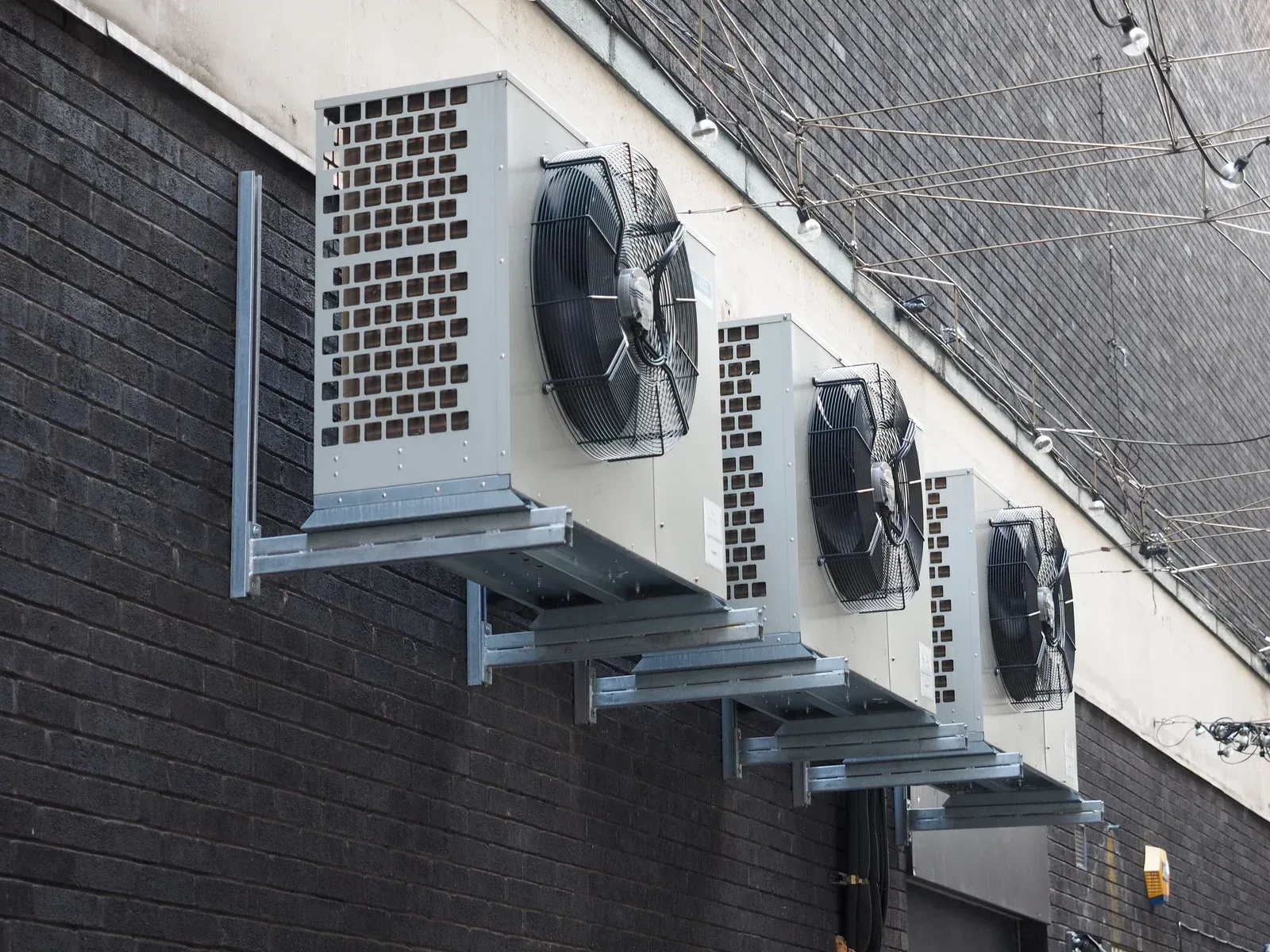 Four air conditioning units mounted on a dark brick wall.
