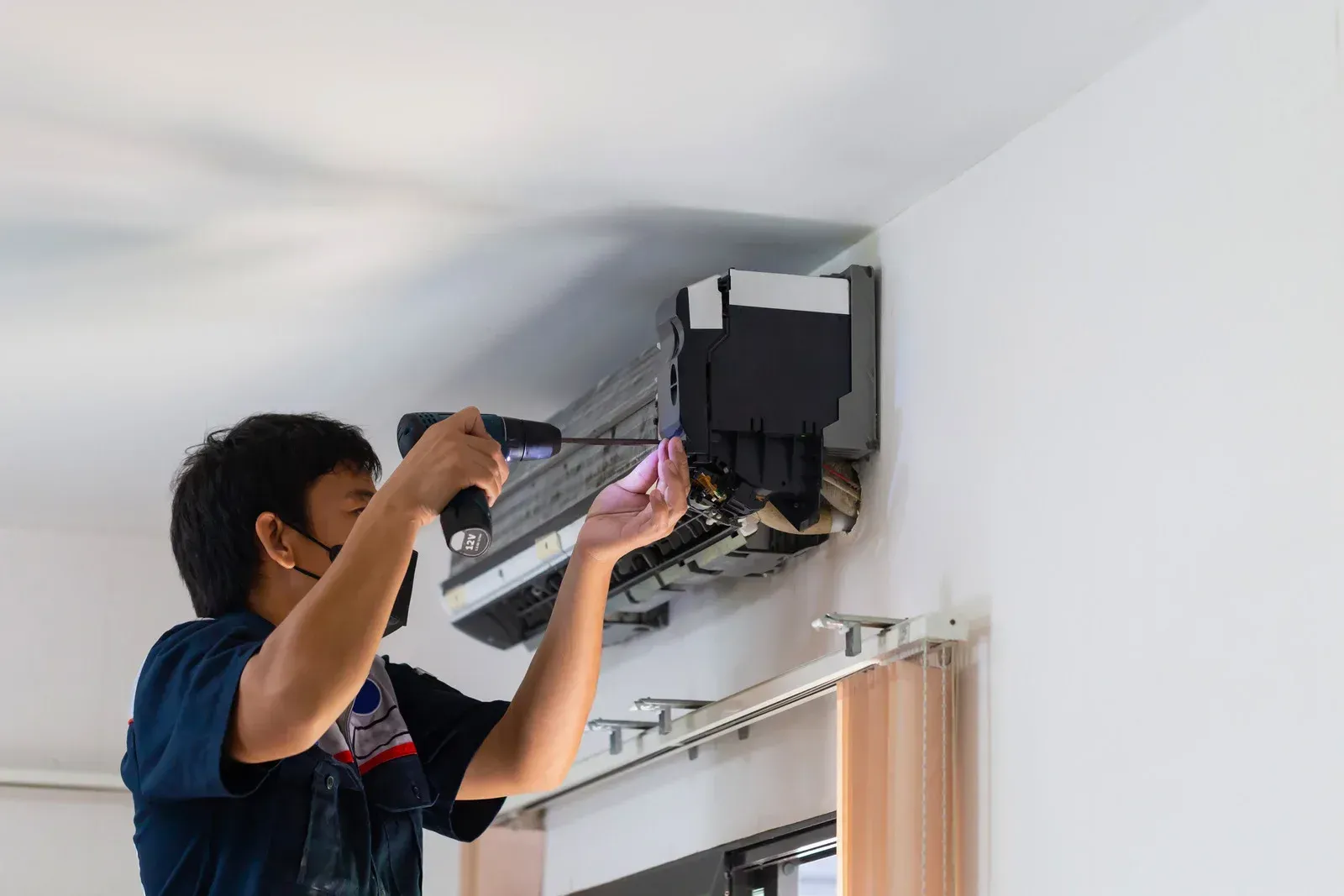 Technician with a drill installing an air conditioner unit on a white wall.