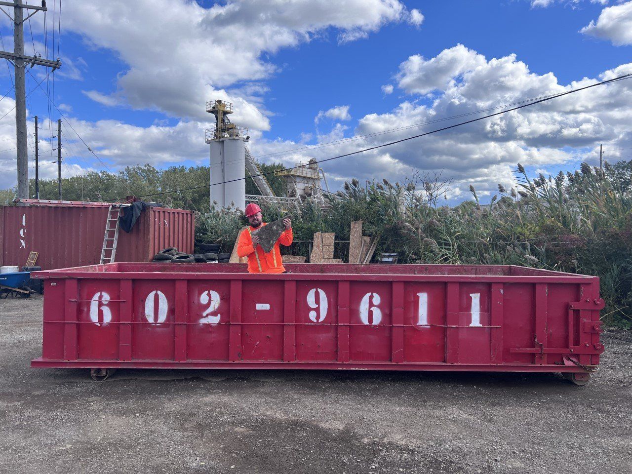 Red construction dumpster with 602-961 on side, a worker in orange, and cloudy sky behind.