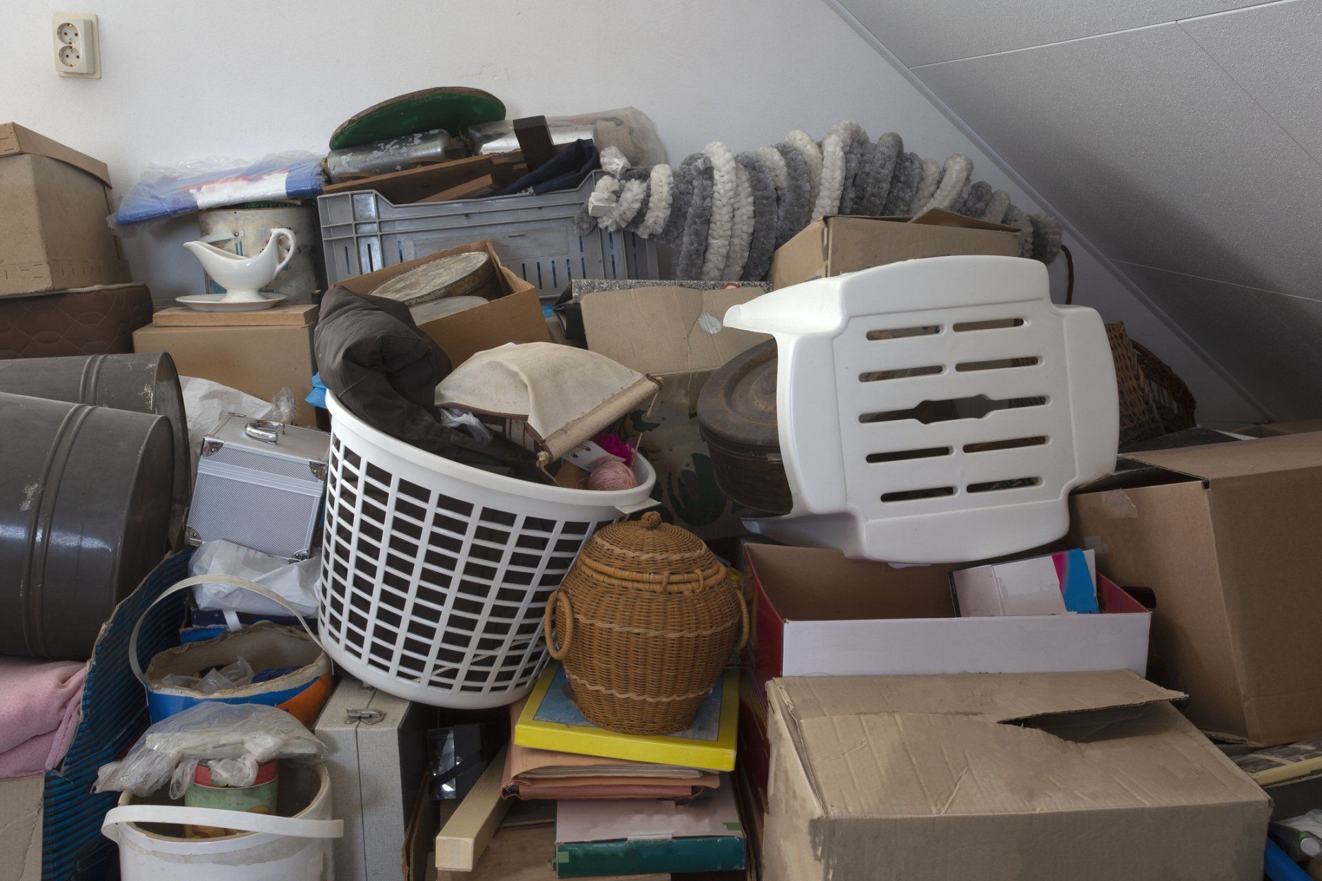 Cluttered attic storage with stacked boxes, laundry baskets, bags, and folded linens under a sloped ceiling