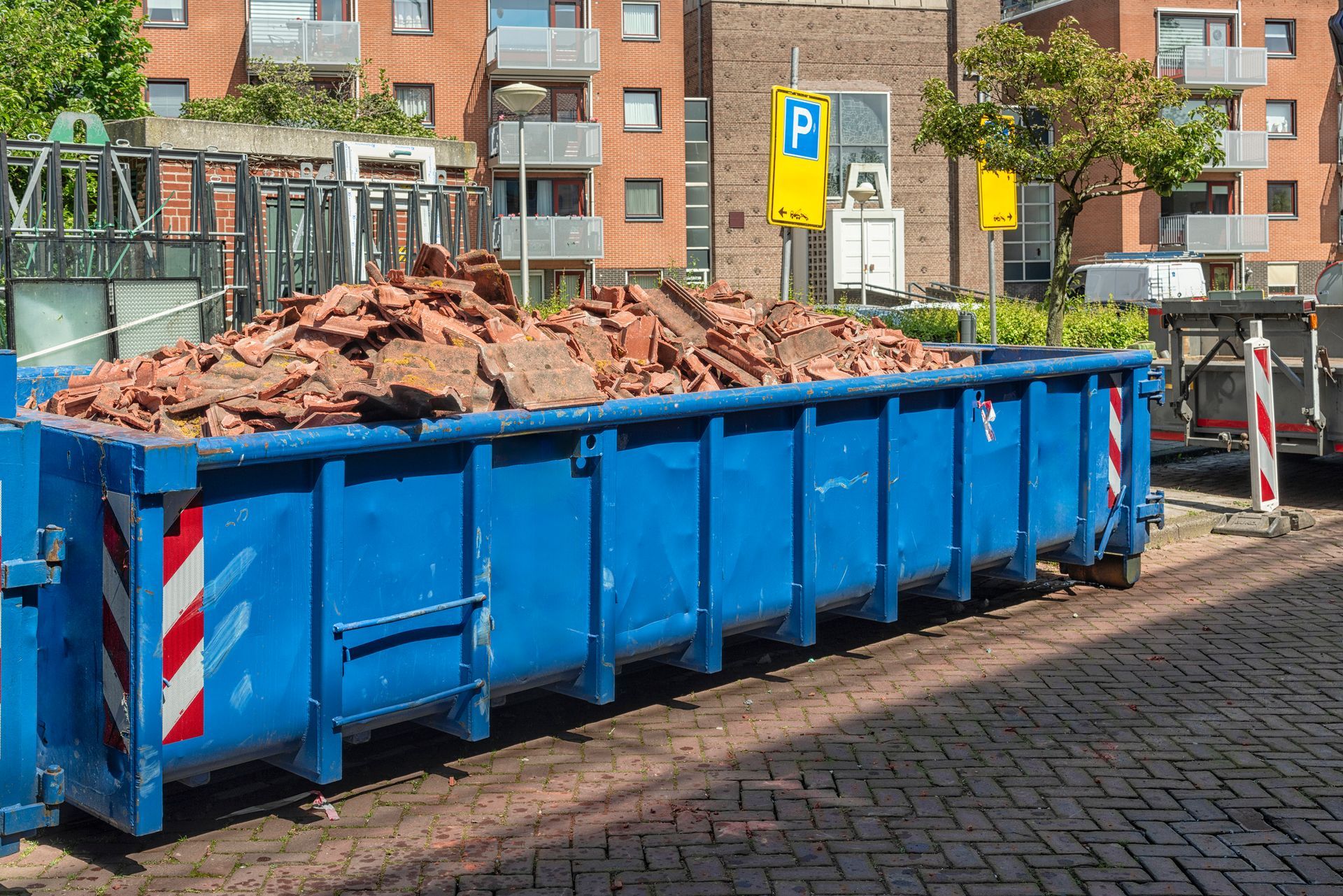 two long blue open industrial steel containers filled with roof tile waste.