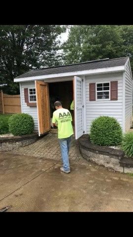 Person opening the door of a small white shed in a driveway after rain