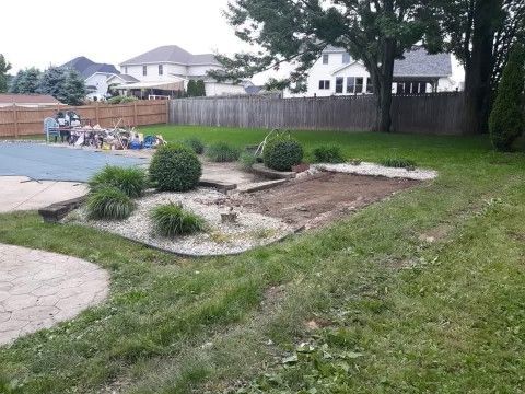 Backyard patio with landscaped flower bed, lawn, fence, and swimming pool in the background