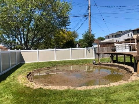 Backyard with a muddy pond, white fence, tree, and wooden deck in the background