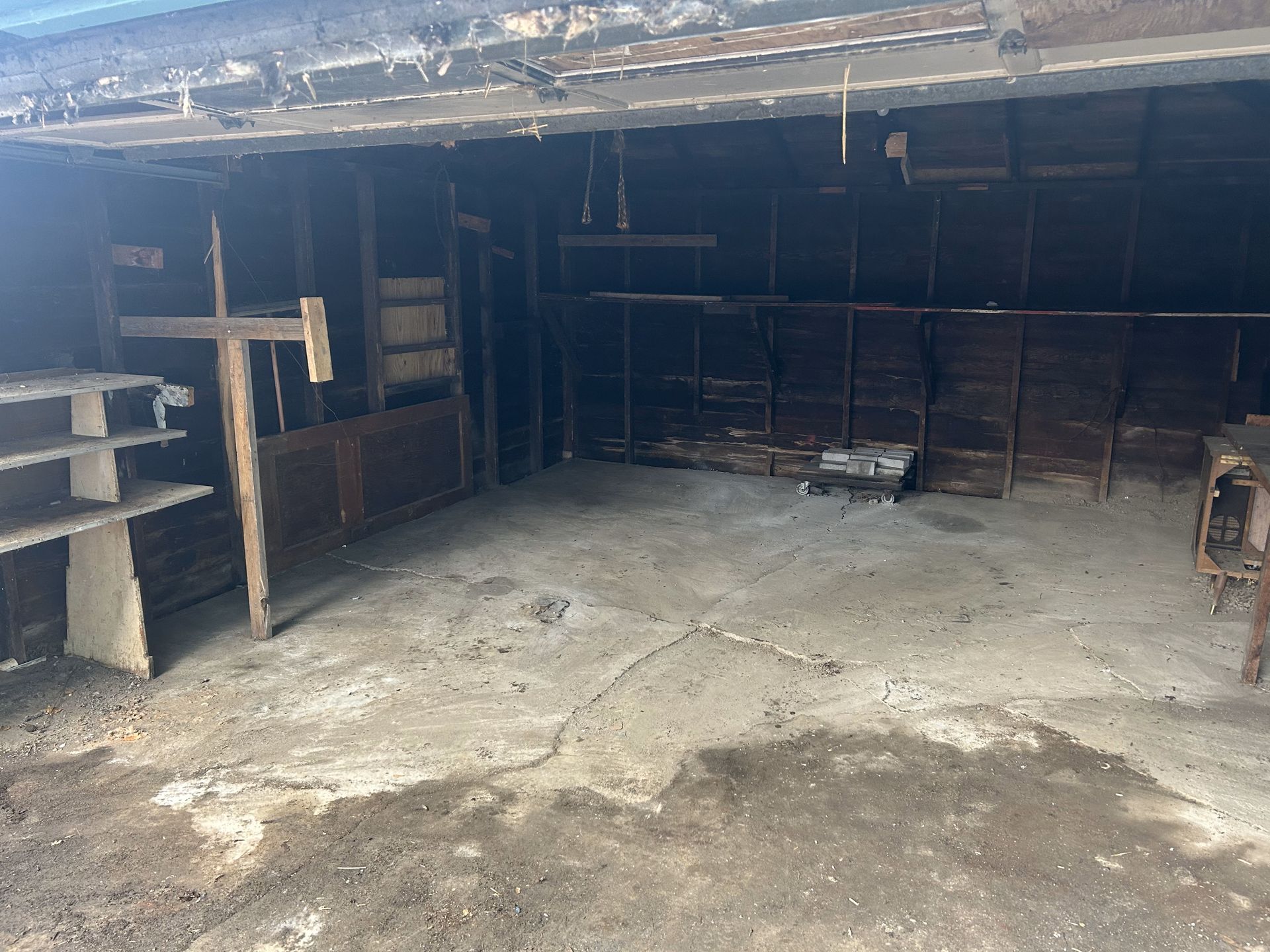 Empty dim garage with concrete floor, wooden shelves on the left, and a dark back wall.