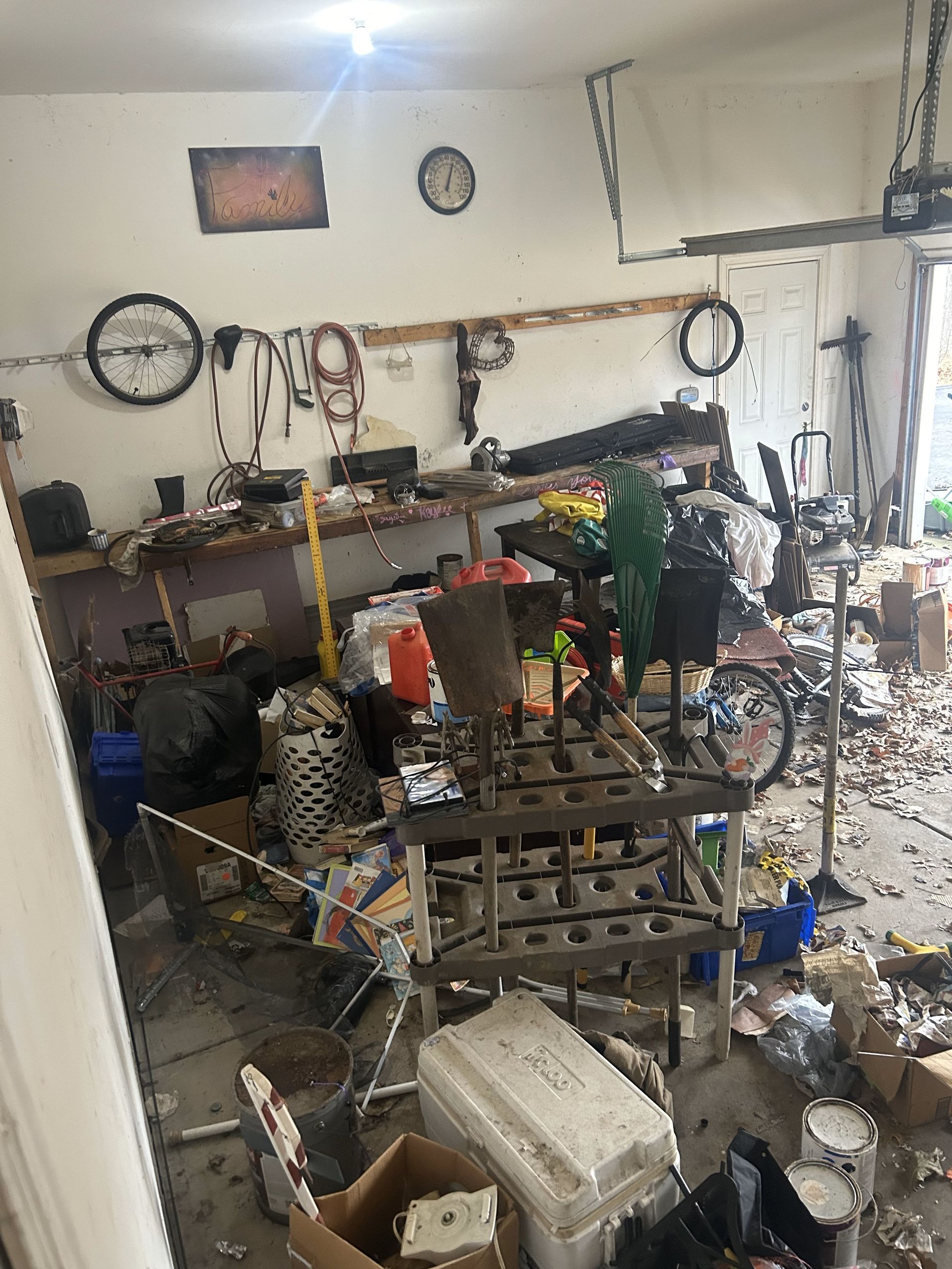 Cluttered garage with tools, boxes, and scattered items on shelves and the floor