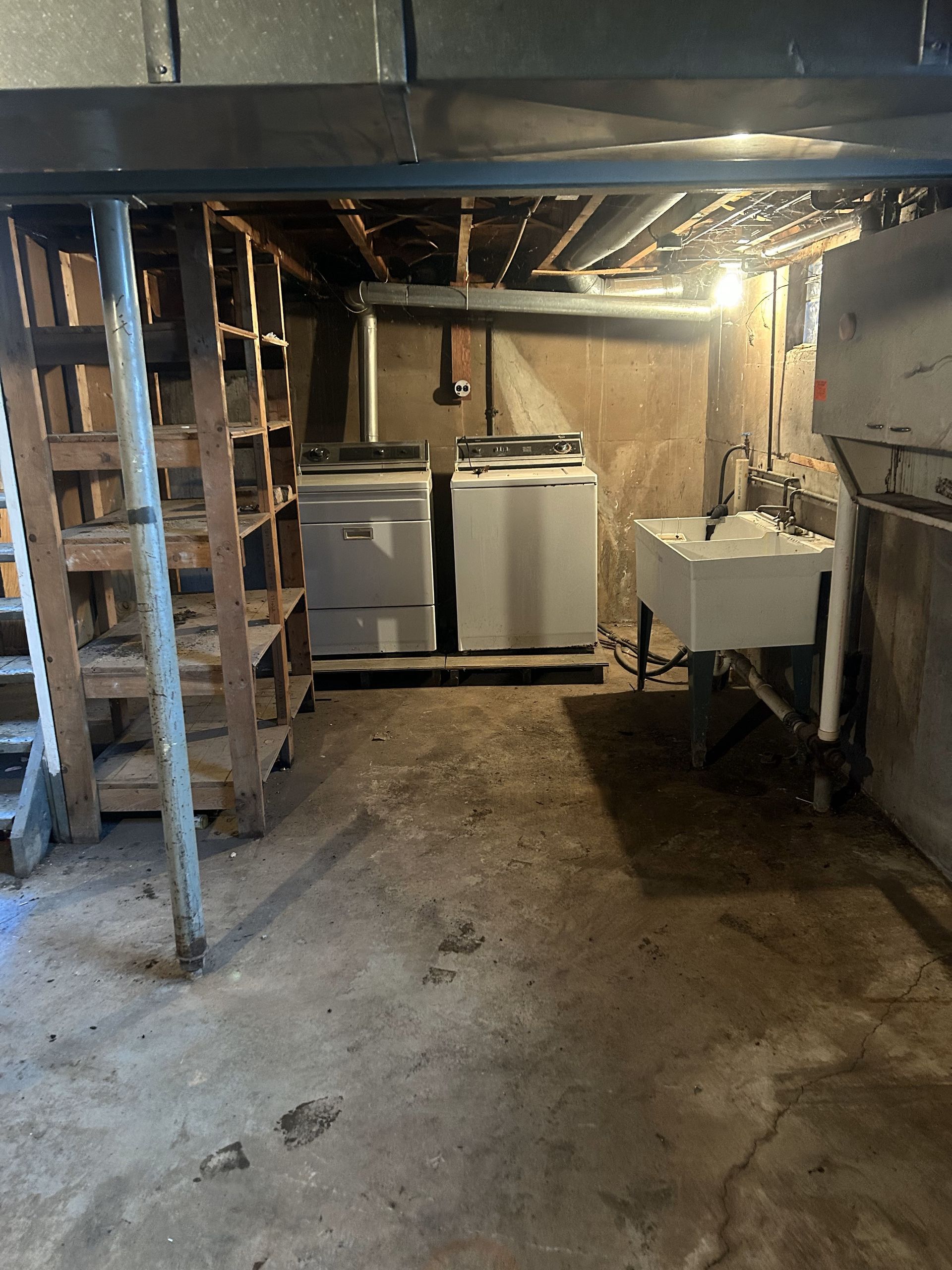 Basement laundry area with two washing machines, utility sink, and exposed beams under low ceiling