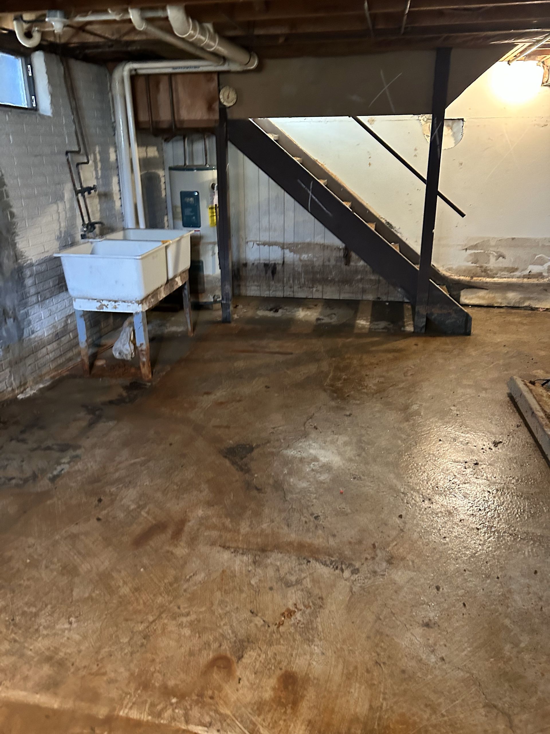 Basement utility area with sink, exposed stairs, and concrete floor under warm light