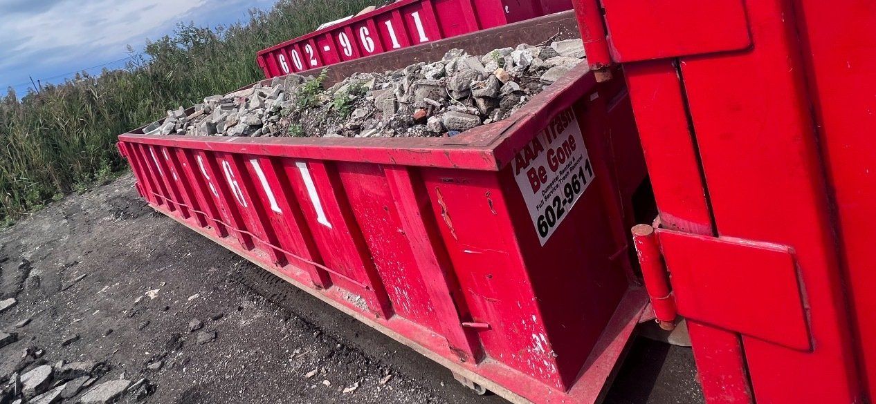 Red dumpster full of rocks beside a gravel pile on a dirt roadside