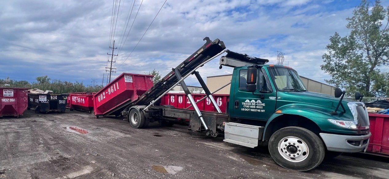 Tow truck loading a red dumpster in a gravel lot under a cloudy sky