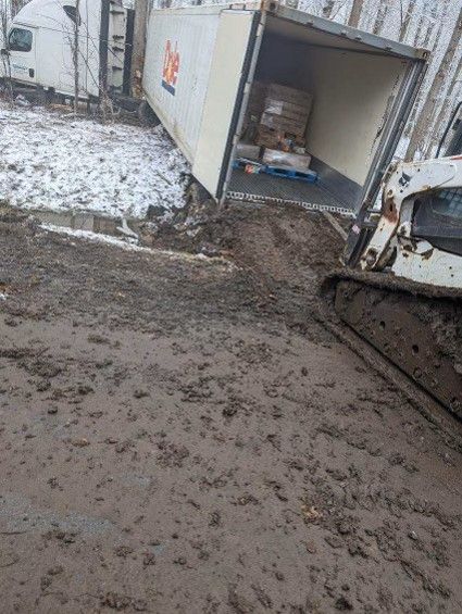 Mud-covered snowy yard with an open shipping container and excavator track