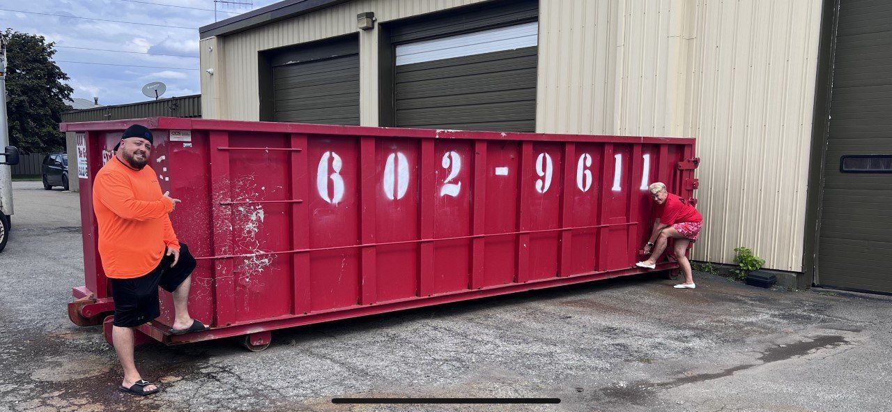 Two people beside a large red dumpster outside an industrial building