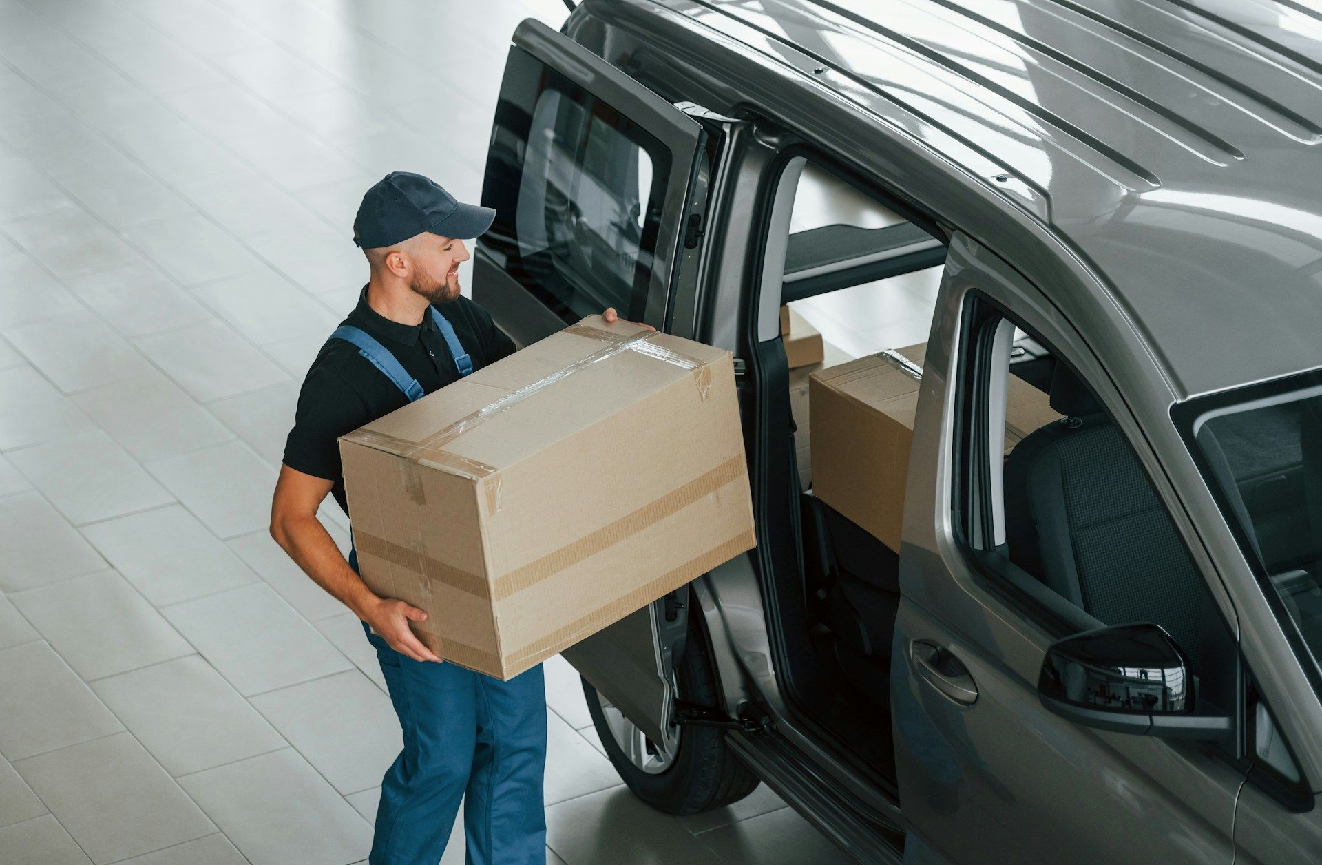 Delivery person carrying a large box from a gray van inside a building.
