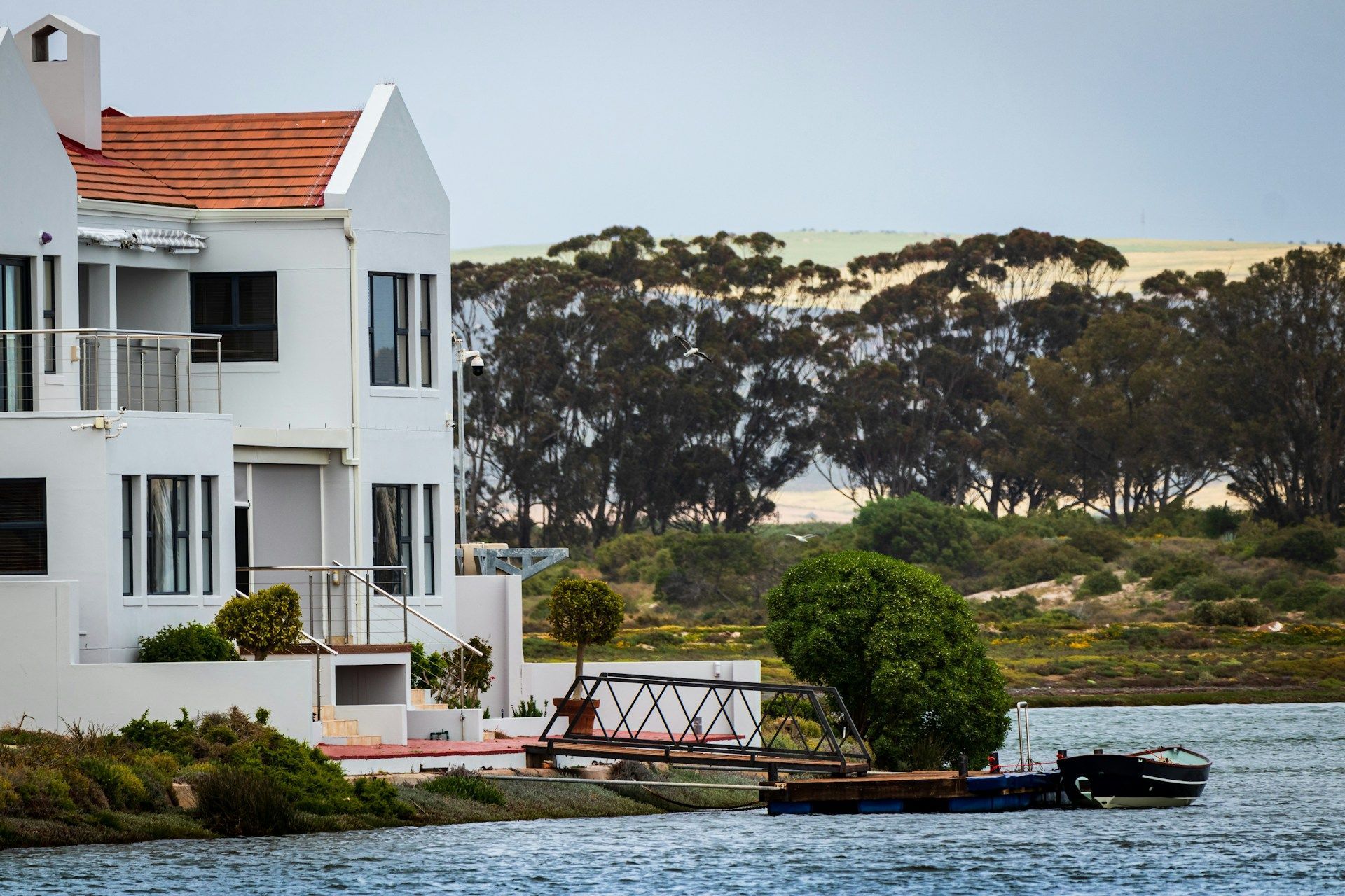 White houses with orange roofs on water's edge, with trees and a sand dune in the background.