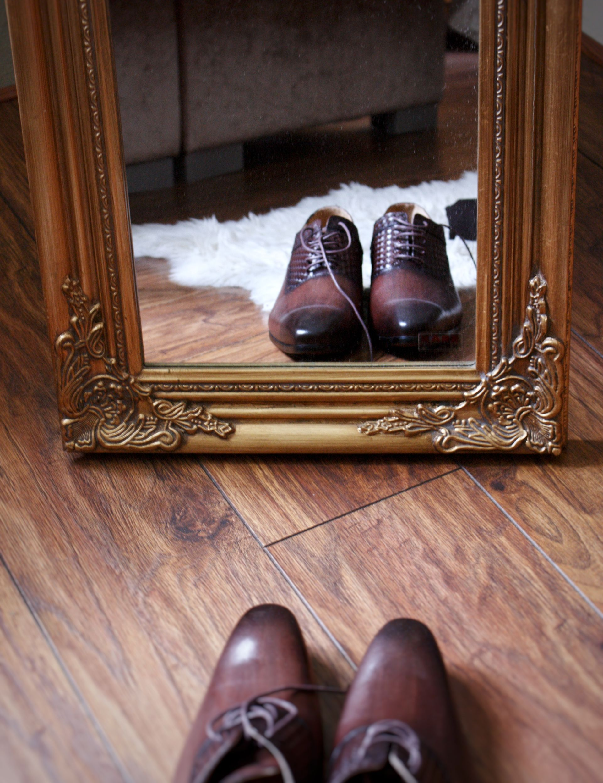 Bruine leren schoenen, weerspiegeld in een sierlijke gouden spiegel, staan ​​op een houten vloer.