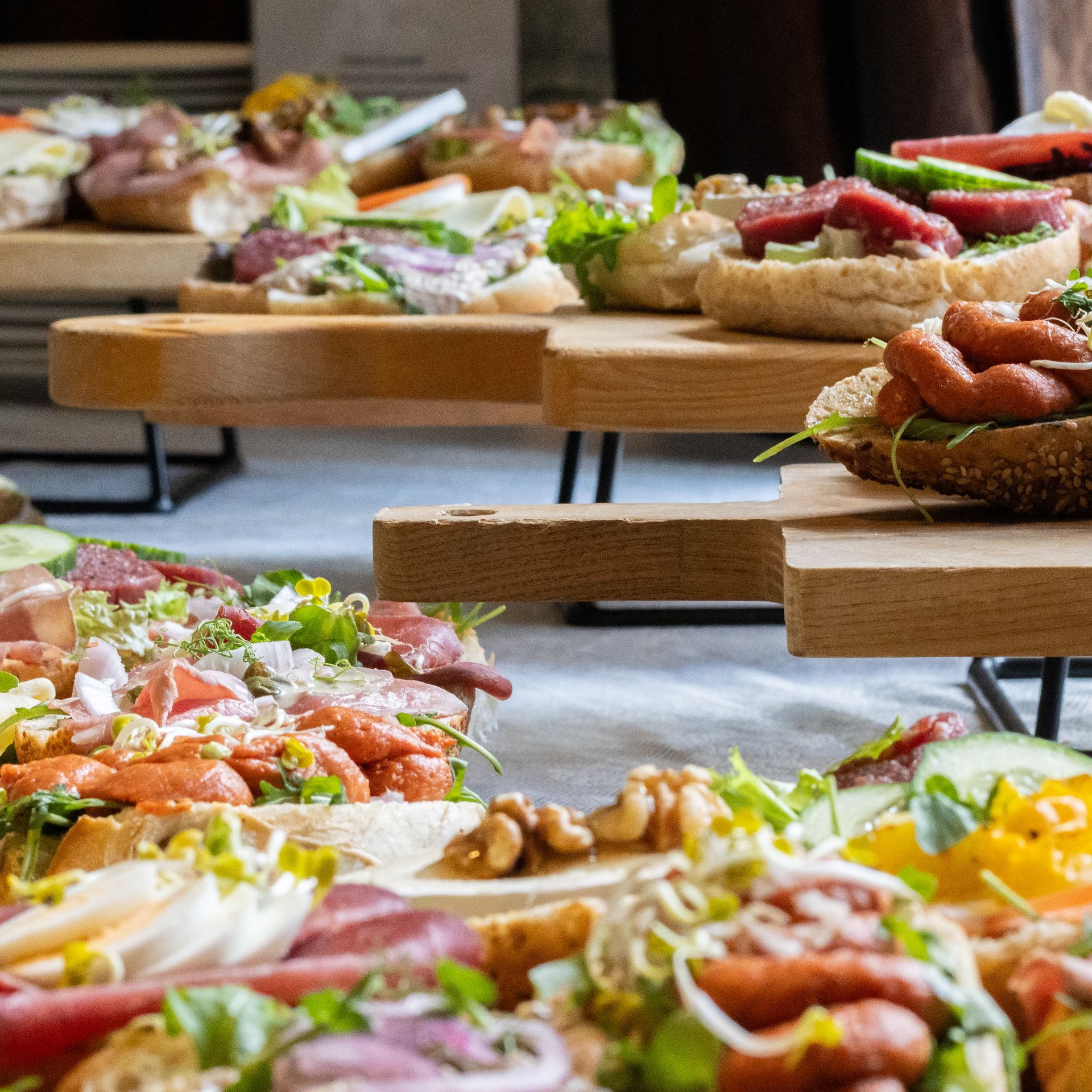 Een assortiment open sandwiches met diverse toppings, geserveerd op houten schalen en uitgestald op een tafel.