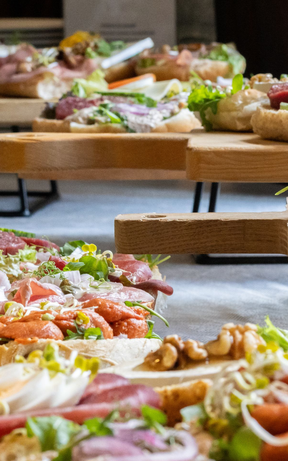 Houten etagères gevuld met diverse sandwiches en beleg voor een cateringevenement.