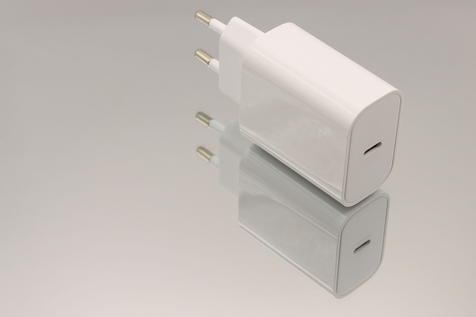 Witte telefoonoplader met EU-stekker, weerspiegeld op een glanzend oppervlak.