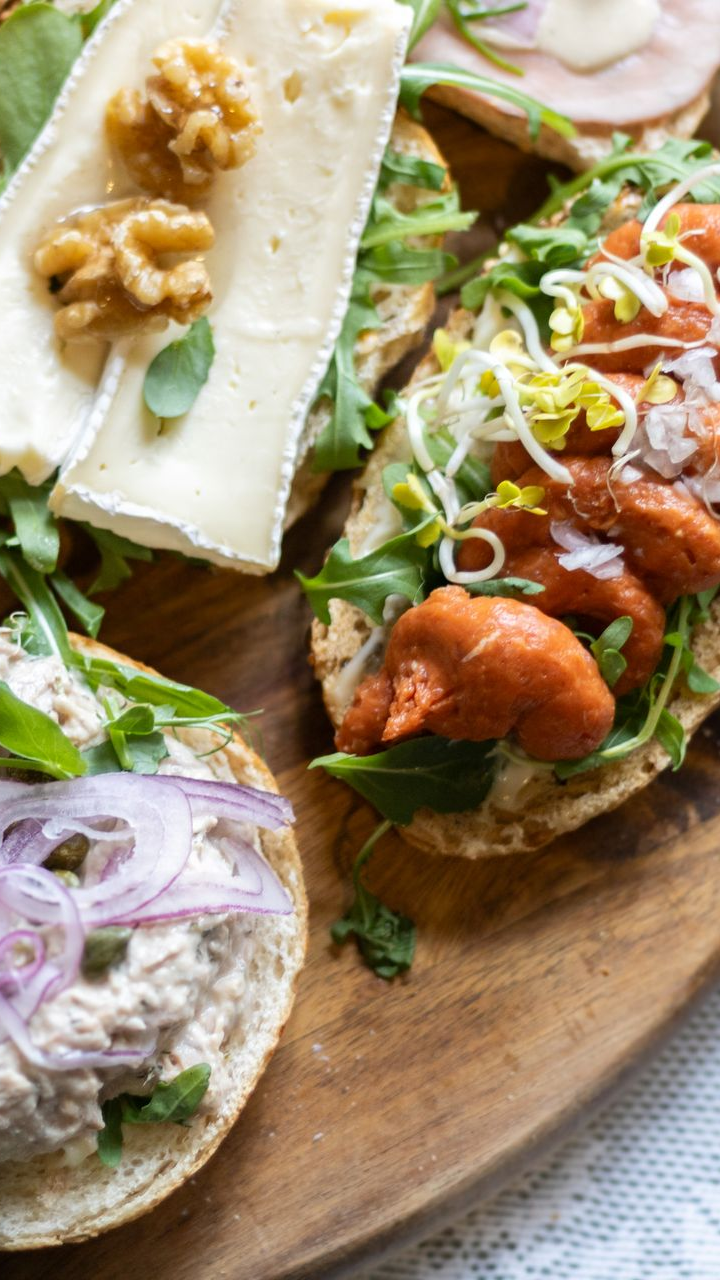 Houten plank met diverse open sandwiches: kaas en walnoten, kreeft en tonijn met rode ui.