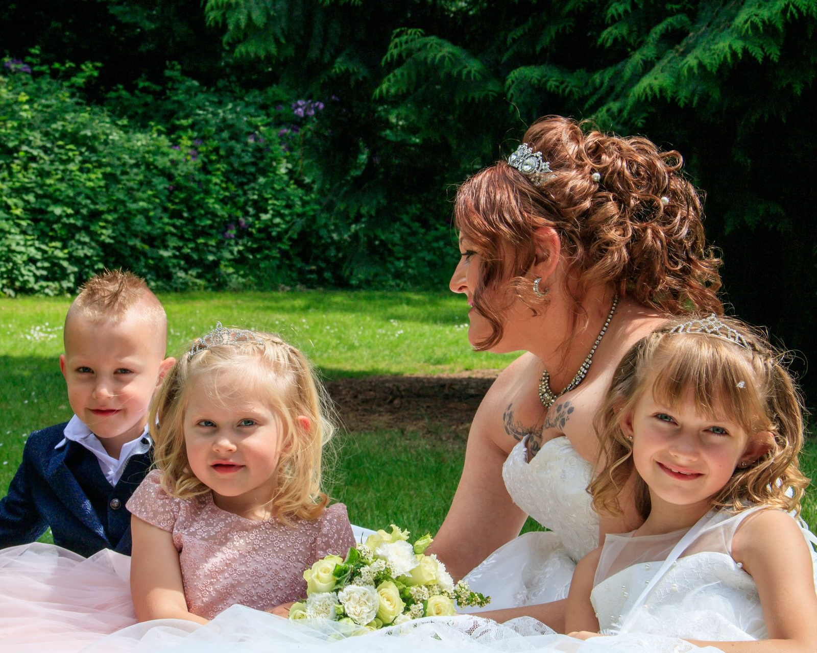 Bruid in een witte jurk met drie kinderen in een tuin. De bruid lacht.