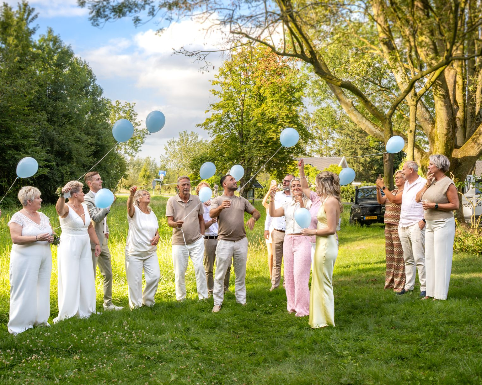 Een groep mensen laat lichtblauwe ballonnen los in een grasveld in de buitenlucht.