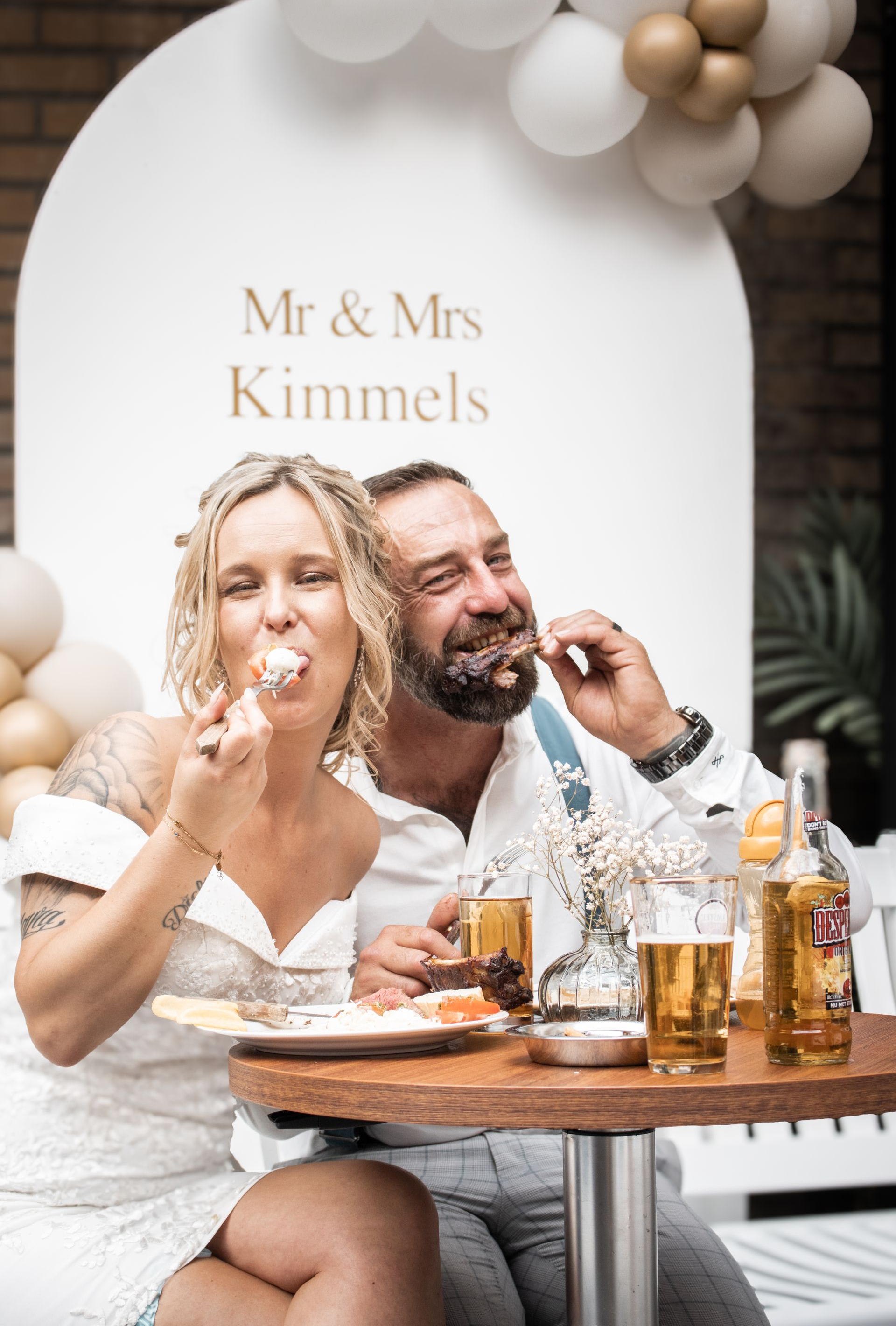 De kersverse echtgenoten, meneer en mevrouw Kimmels, genieten van een stuk taart. Het stel lacht en eet taart. Witte achtergrond met ballonnen.