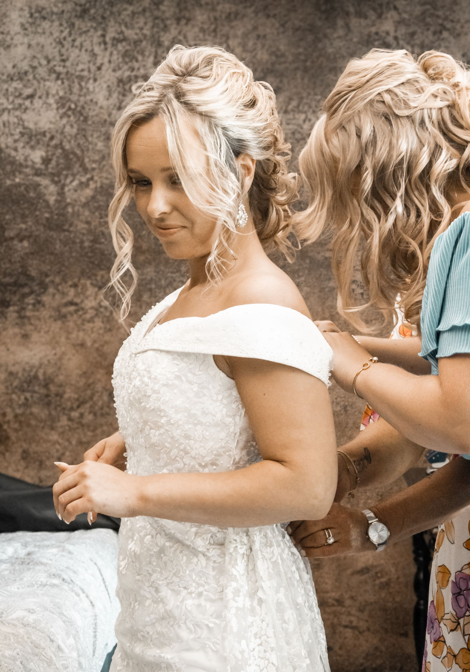 Vrouw in witte jurk, met gestyled haar, laat haar jurk door een andere vrouw verstellen.