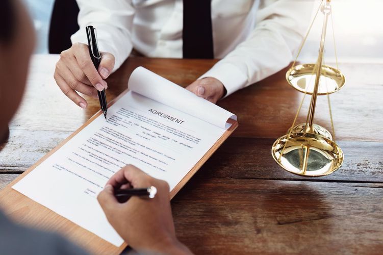 Lawyer pointing at a document, client signing. 