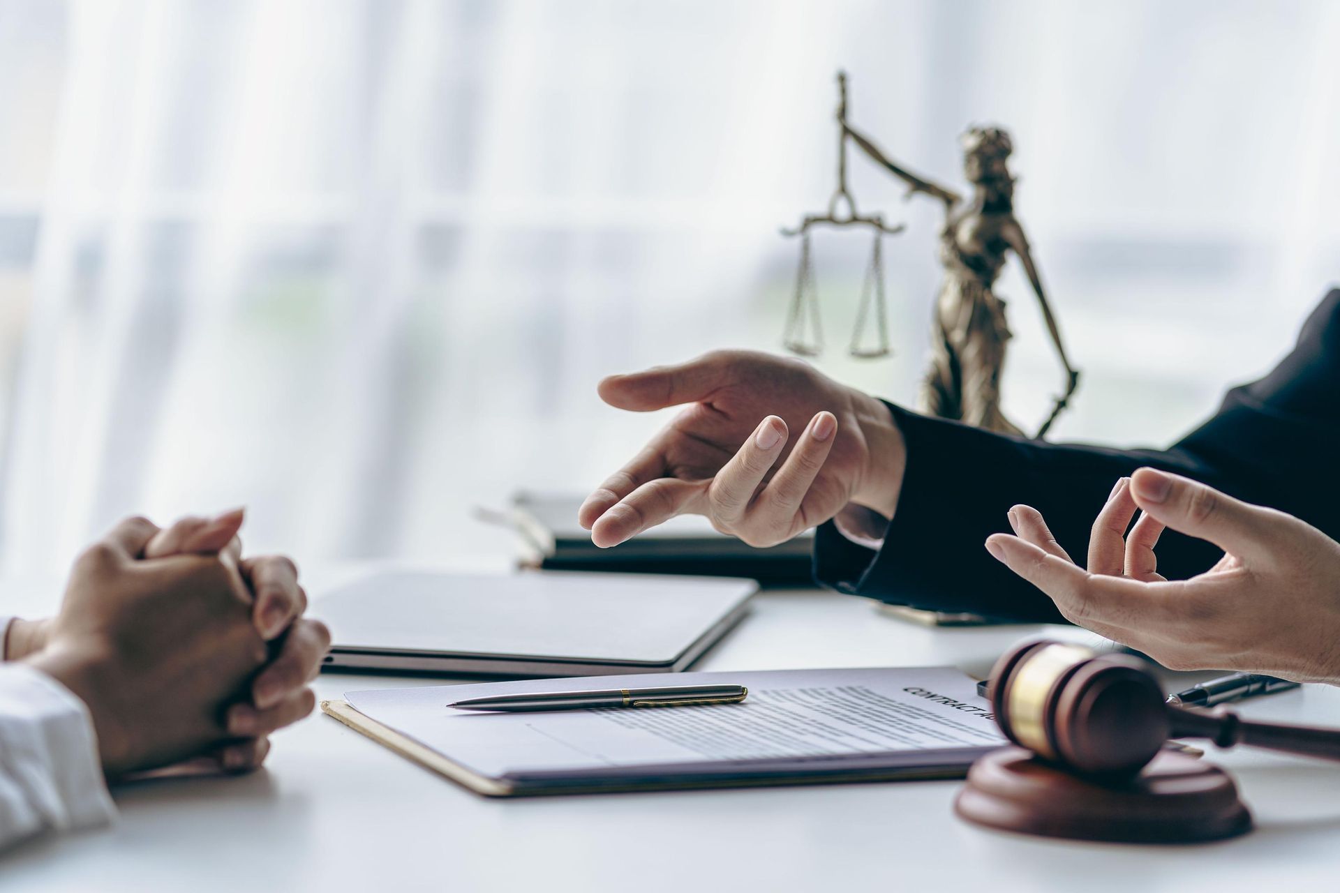 Two people, one in a suit, talking over documents with a gavel and scales of justice on a desk.