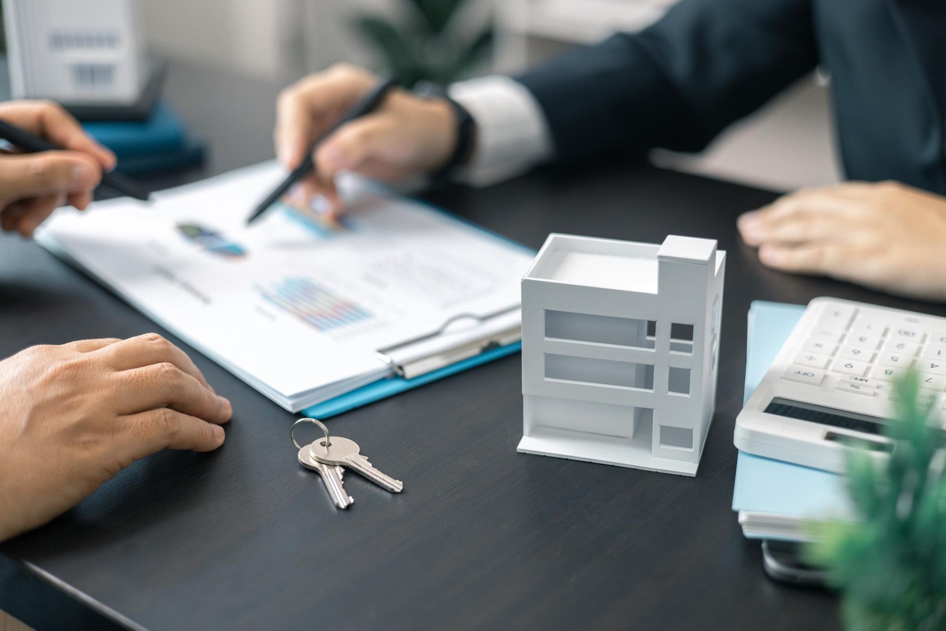 People reviewing documents, house keys, miniature building model, calculator.