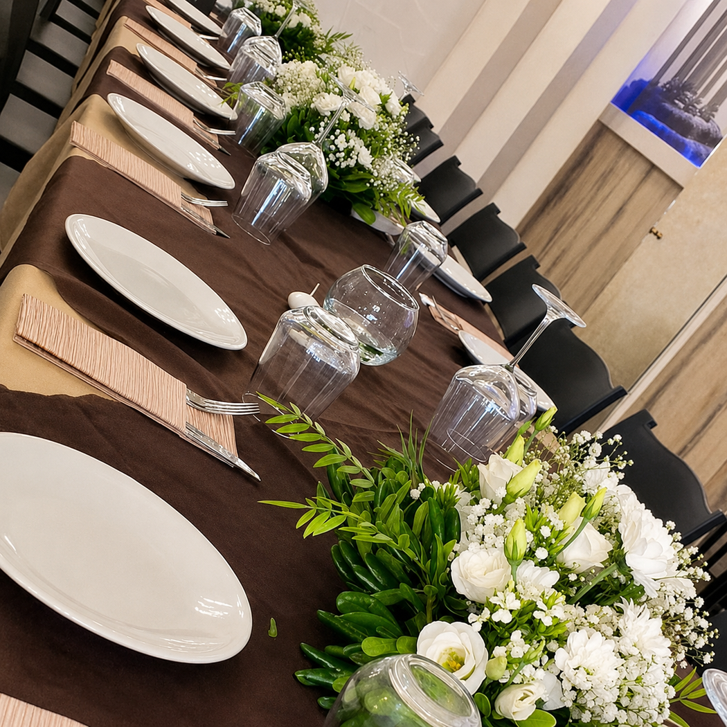 Elegante tavolo da banchetto apparecchiato con piatti bianchi, bicchieri e centrotavola floreali bianchi in una sala da pranzo moderna.