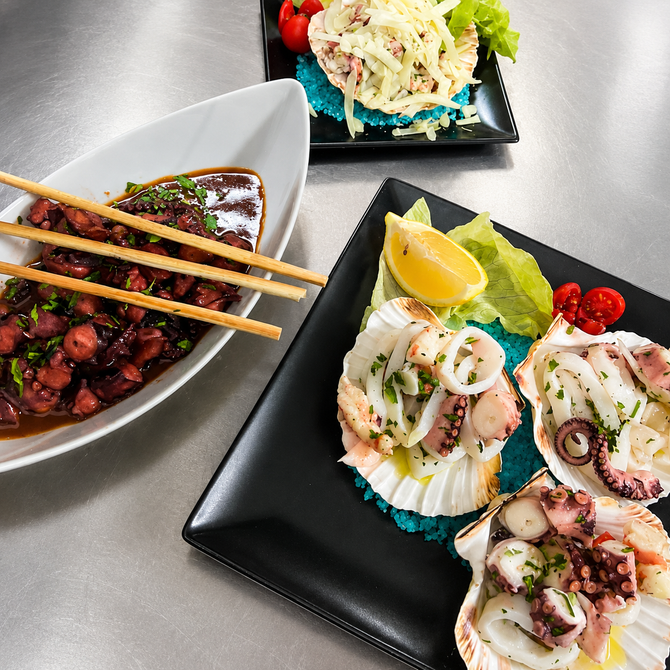Assortimento di sushi e piatti di pesce su piatti neri con bacchette su un tavolo in acciaio inox.
