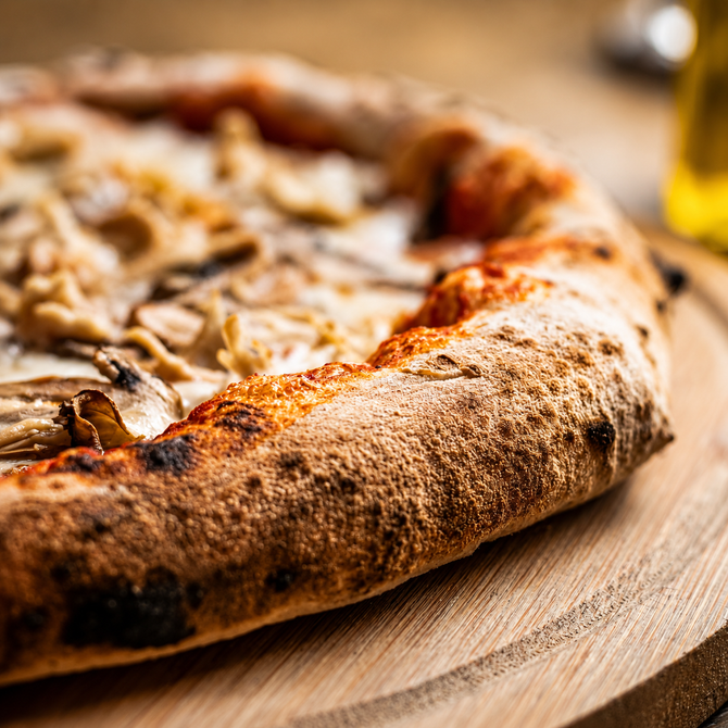Primo piano di una pizza rustica cotta nel forno a legna su un tagliere di legno, con una crosta dorata.