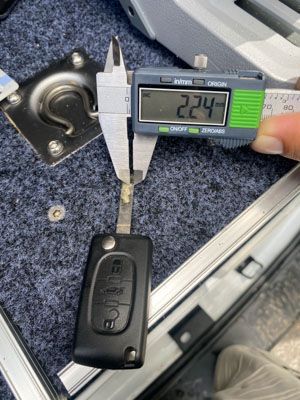 A person is measuring the length of a car key with a digital caliper.